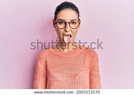 Young caucasian woman wearing casual clothes and glasses sticking tongue out happy with funny expression. emotion concept. 