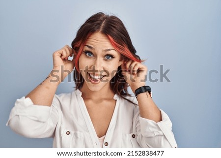 Young caucasian woman wearing casual white shirt over isolated background smiling pulling ears with fingers, funny gesture. audition problem 