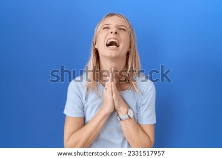 Young caucasian woman wearing casual blue t shirt begging and praying with hands together with hope expression on face very emotional and worried. begging. 