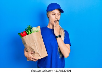 Young Caucasian Woman Wearing Courier Uniform With Groceries From Supermarket Bored Yawning Tired Covering Mouth With Hand. Restless And Sleepiness. 