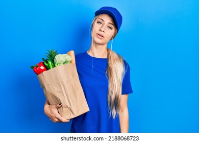 Young Caucasian Woman Wearing Courier Uniform With Groceries From Supermarket Looking Sleepy And Tired, Exhausted For Fatigue And Hangover, Lazy Eyes In The Morning. 