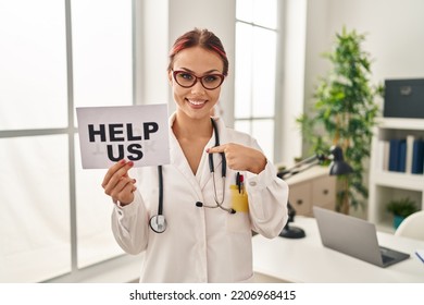 Young Caucasian Woman Wearing Doctor Uniform Holding Help Us Banner Pointing Finger To One Self Smiling Happy And Proud 