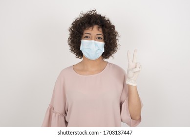 Young caucasian woman wearing face mask standing against gray wall showing and pointing up with fingers number two while smiling confident and happy.