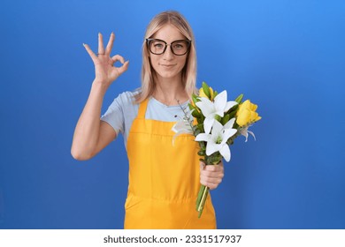 Young caucasian woman wearing florist apron holding flowers smiling positive doing ok sign with hand and fingers. successful expression.  - Powered by Shutterstock