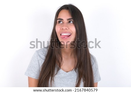 young caucasian woman wearing grey t-shirt over white background showing grimace face crossing eyes and showing tongue. Being funny and crazy