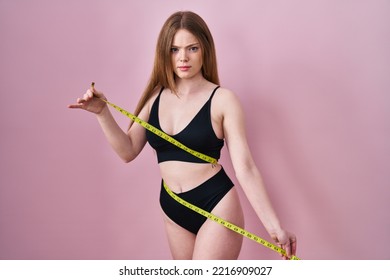 Young Caucasian Woman Wearing Lingerie Using Tape Measure Skeptic And Nervous, Frowning Upset Because Of Problem. Negative Person. 