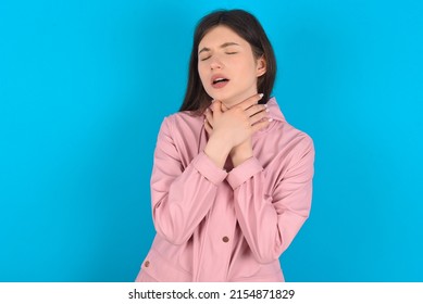 Young caucasian woman wearing pink raincoat over blue background shouting suffocate because painful strangle. Health problem. Asphyxiate and suicide concept.