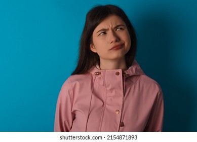 Young caucasian woman wearing pink raincoat over blue background making grimace and crazy face, screaming out of control, funny lunatic expressing freedom and wild.