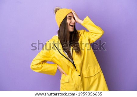 Young caucasian woman wearing a rainproof coat isolated on purple background smiling a lot