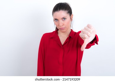 Young Caucasian Woman Wearing Red Shirt Over White Background Feeling Angry, Annoyed, Disappointed Or Displeased, Showing Thumbs Down With A Serious Look