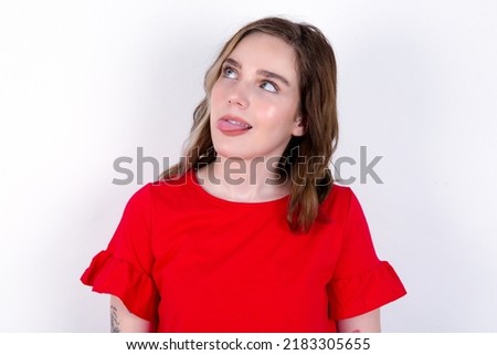 young caucasian woman wearing red T-shirt over white background  showing grimace face crossing eyes and showing tongue. Being funny and crazy