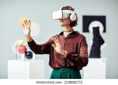 Young Caucasian woman wearing VR headset looking at art objects while visiting modern exhibition using augmented reality technology - Powered by Shutterstock