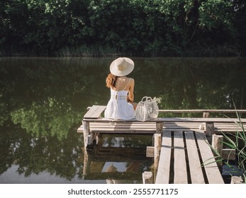 Young Caucasian woman in a white dress and hat sitting on a wooden dock by a calm lake, enjoying a peaceful moment. Ideal for concepts of relaxation, nature, and summer serenity. Great for - Powered by Shutterstock