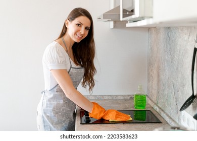 Young caucasian woman wiping an electric stove with a textile wipe while working in a modern kitchen at home. Cleaning service concept. Housework. Cleaning lady at work