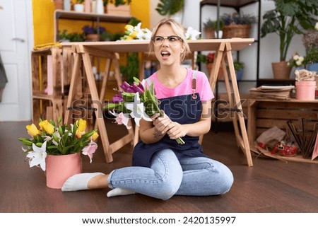 Young caucasian woman working at florist shop sitting of floor angry and mad screaming frustrated and furious, shouting with anger. rage and aggressive concept. 