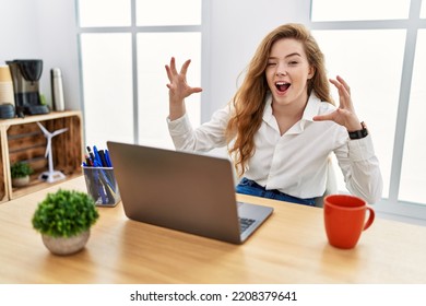 Young Caucasian Woman Working At The Office Using Computer Laptop Shouting Frustrated With Rage, Hands Trying To Strangle, Yelling Mad 