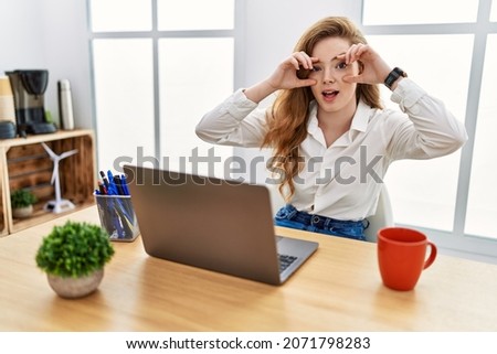 Young caucasian woman working at the office using computer laptop trying to open eyes with fingers, sleepy and tired for morning fatigue 