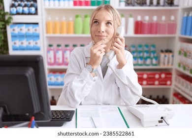 Young caucasian woman working at pharmacy drugstore speaking on the telephone looking confident at the camera smiling with crossed arms and hand raised on chin. thinking positive.  - Powered by Shutterstock