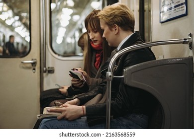 Young Caucasian Women Sitting In Subway Carriage Looking At Smartphone. Image With Selective Focus, Toning And Noise Effect