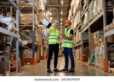 young Caucasian workers in uniform make an inventory management of products on shelves in warehouse, discuss together. Concept of good management system to support working with industrial business. - Powered by Shutterstock