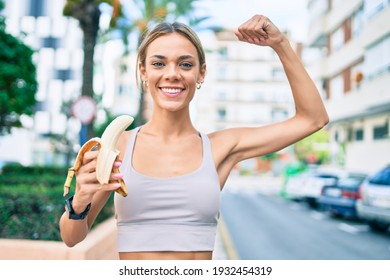 Young Cauciasian Fitness Woman Wearing Sport Clothes Training Outdoors Eating Healthy Banana And Showing Proud Arm Muscle