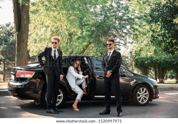 Young celebrity getting out of car surrounded\
by bodyguards