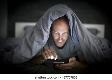 A Young Cell Phone Addict Man Awake Late At Night In Bed Using Smartphone