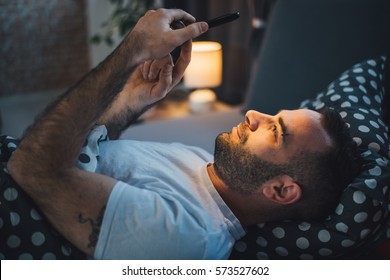 Young Cell Phone Addict Man Awake At Night In Bed Using Smartphone For Chatting, Flirting And Sending Text Message In Internet Addiction And Mobile Abuse Concept