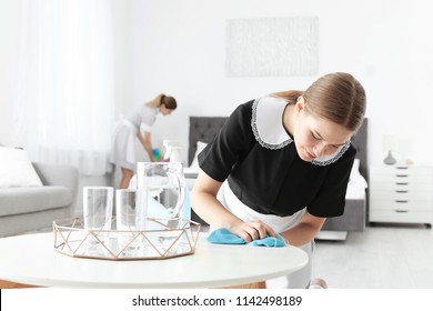 Young Chambermaid Cleaning Table In Hotel Room