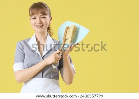 Young chambermaid with dustpan and brush on yellow background
