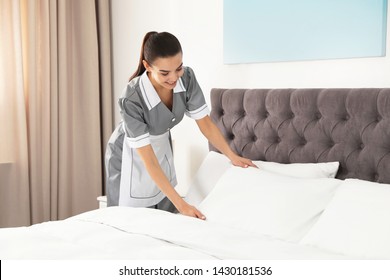 Young Chambermaid Making Bed In Hotel Room. Space For Text