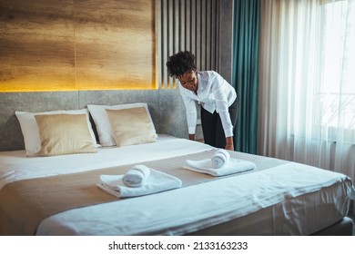 Young Chambermaid Making Bed In Hotel Room. Young Hotel Maid Setting Up White Pillow On Bed Sheet In Hotel Room. Young Maid Arranging Blanket On Bed In Hotel Room