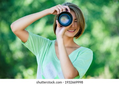 Young Charming Calm Woman In A Green Blouse Takes Pictures On A Camera With A Large Lens In The Summer Park.