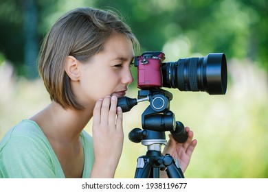 Junge charmante, ruhige Frau in einer grünen Bluse fotografiert auf einer roten Kamera mit einem großen Objektiv im Sommerpark.