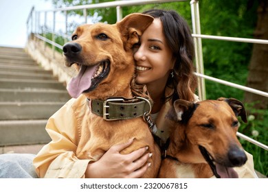 Young charming smiling girl is resting while walking in the park with two golden dogs. The girl hugs her pets. Love and affection between owner and pet. Adopting a pet from a shelter.