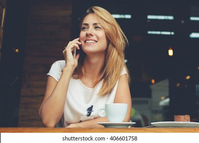 Young charming woman calling with cell telephone while sitting alone in coffee shop during free time, attractive female with cute smile having talking conversation with mobile phone while rest in cafe