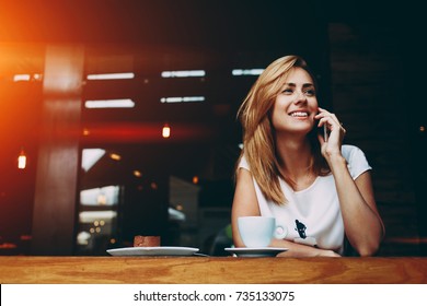 Young Charming Woman Calling With Cell Telephone While Sitting Alone In Coffee Shop During Free Time, Attractive Female With Cute Smile Having Talking Conversation With Mobile Phone While Rest In Cafe