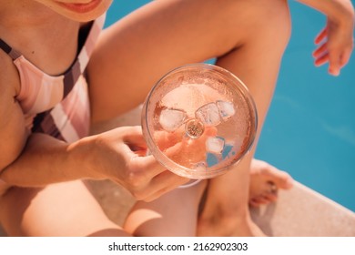 Young charming  woman chilling near swimming pool and drinking rose wine at sunset. Luxury lifestyle content. Top view picture.