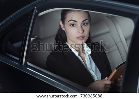 Young charming woman in suit  sitting in backseat of car with digital tablet