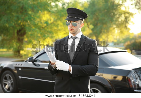 Young chauffeur adjusting gloves near luxury car\
on the street