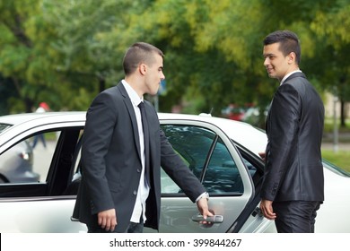 Young Chauffeur Is Holding The Door For The Young Businessman Getting Into The Car