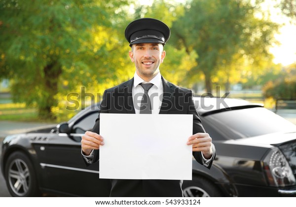 Young chauffeur standing with white board near\
luxury car on the street
