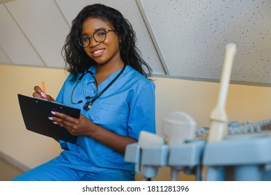 Young cheerful African woman operator of an ultrasound scanning machine analyzing diagnostics results of patient. Young smiling African doctor working on a modern ultrasound equipment. - Shutterstock ID 1811281396