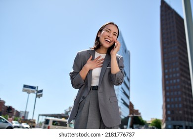Young cheerful Asian successful businesswoman wearing suit standing on city street talking on mobile phone. Smiling woman making business call on cell feeling happy about good news outdoors. - Shutterstock ID 2181776737