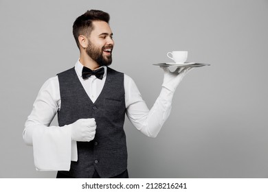 Young Cheerful Barista Male Waiter Butler Man Wear White Shirt Vest Elegant Uniform Work At Cafe Hold Plate Coffee Cup Isolated On Plain Grey Background Studio Portrait. Restaurant Employee Concept