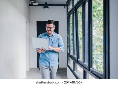 Young Cheerful Beautiful Joyful Man Manager Businessman Entrepreneur Small Business Owner Employee Worker With Glasses Smiling While Working With His Laptop Walking In Office Hallway Corridor