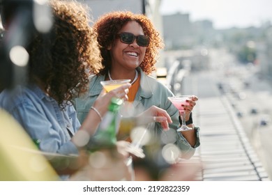 Young Cheerful Black Woman With Cocktail Enjoying Gathering With Friends In Outdoor Cafe While Having Chat With Friend On Rooftop