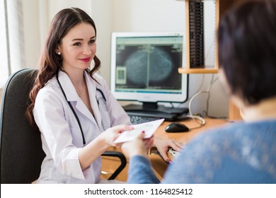 The young cheerful breast specialist sitting with the patient in her office and giving a disc with ultrasound examination