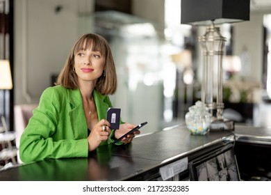 Young And Cheerful Business Woman Stands With Card Key And Phone At The Reception Of Luxury Hotel. Woman Check In Hotel During A Business Trip