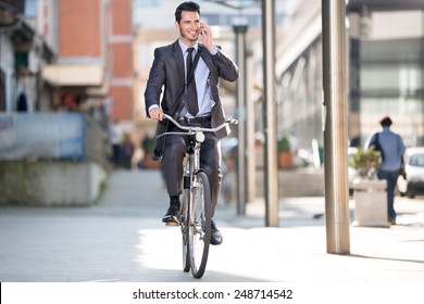 Young cheerful businessman riding a bicycle and using phone go to work  - Powered by Shutterstock